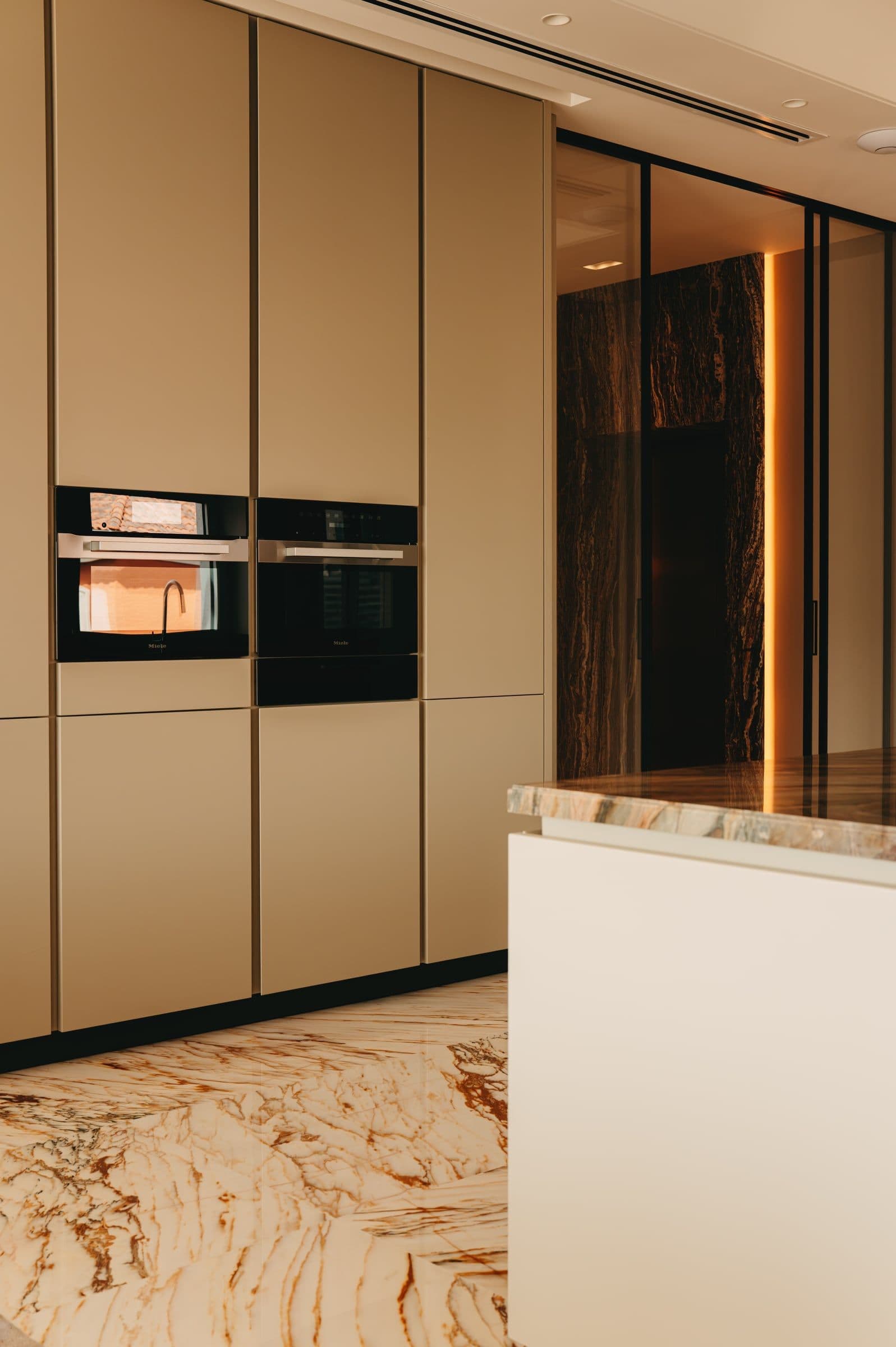 A kitchen with built-in ovens in bronze-toned cabinetry beside an onyx-clad island.