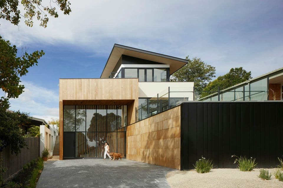 A contemporary house clad in timber and dark metal, photographed from the driveway in full sun.