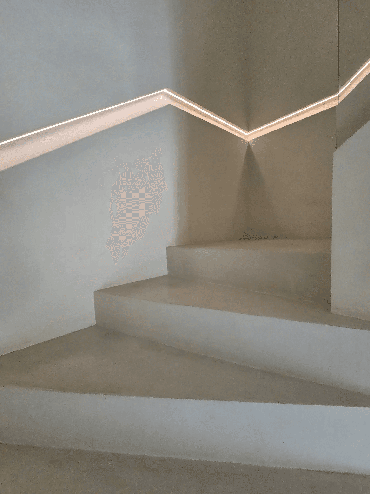 A plastered staircase turning through a quarter landing, lit by a recessed strip that follows the handrail.