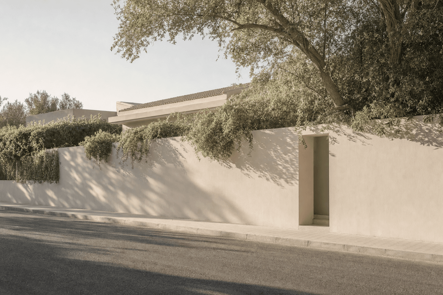 A low plaster boundary wall under mature trees along a quiet residential street, with a doorway cut into it.