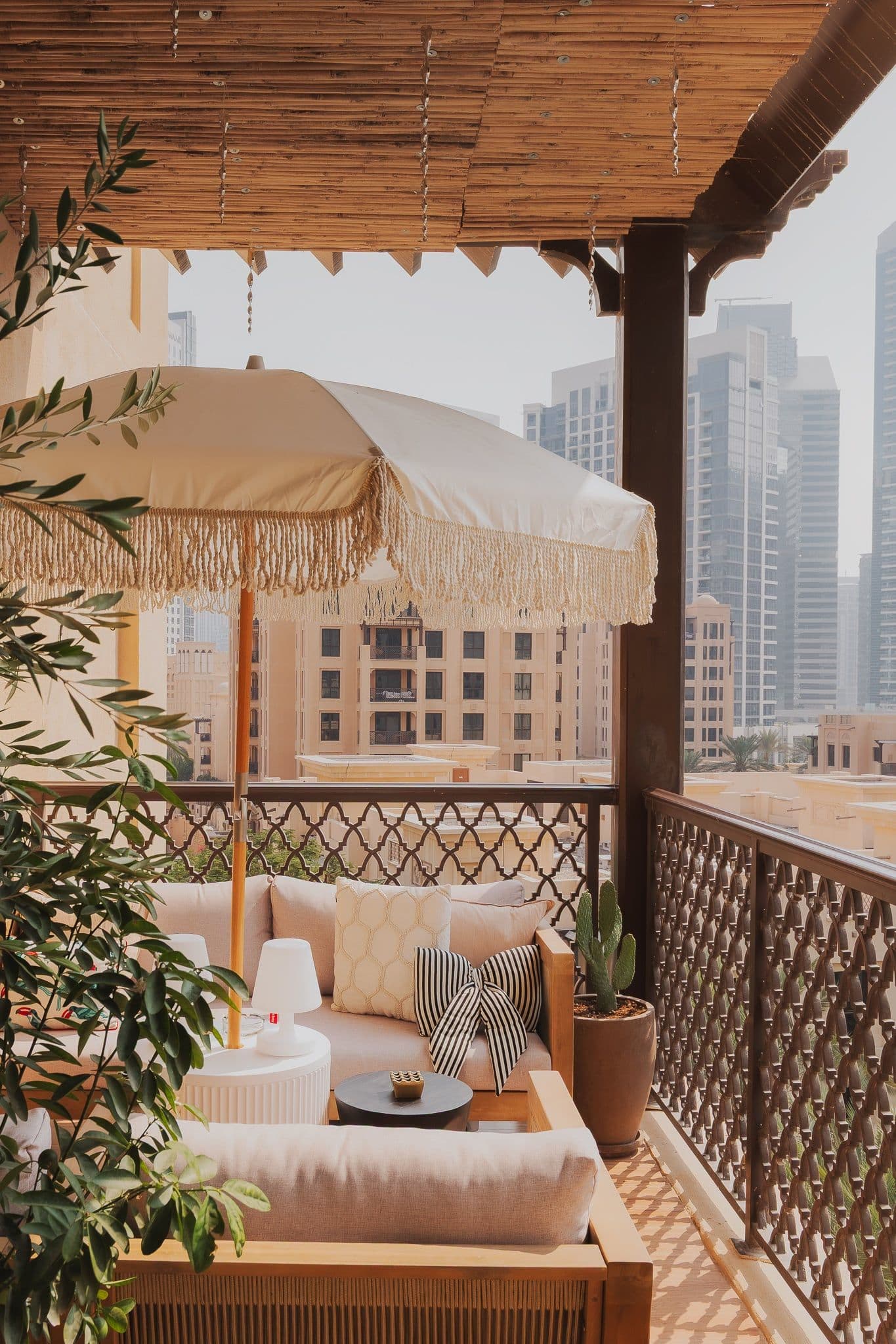 A shaded balcony with a fringed parasol, cushioned seating and a lattice balustrade, with Downtown Dubai towers beyond.