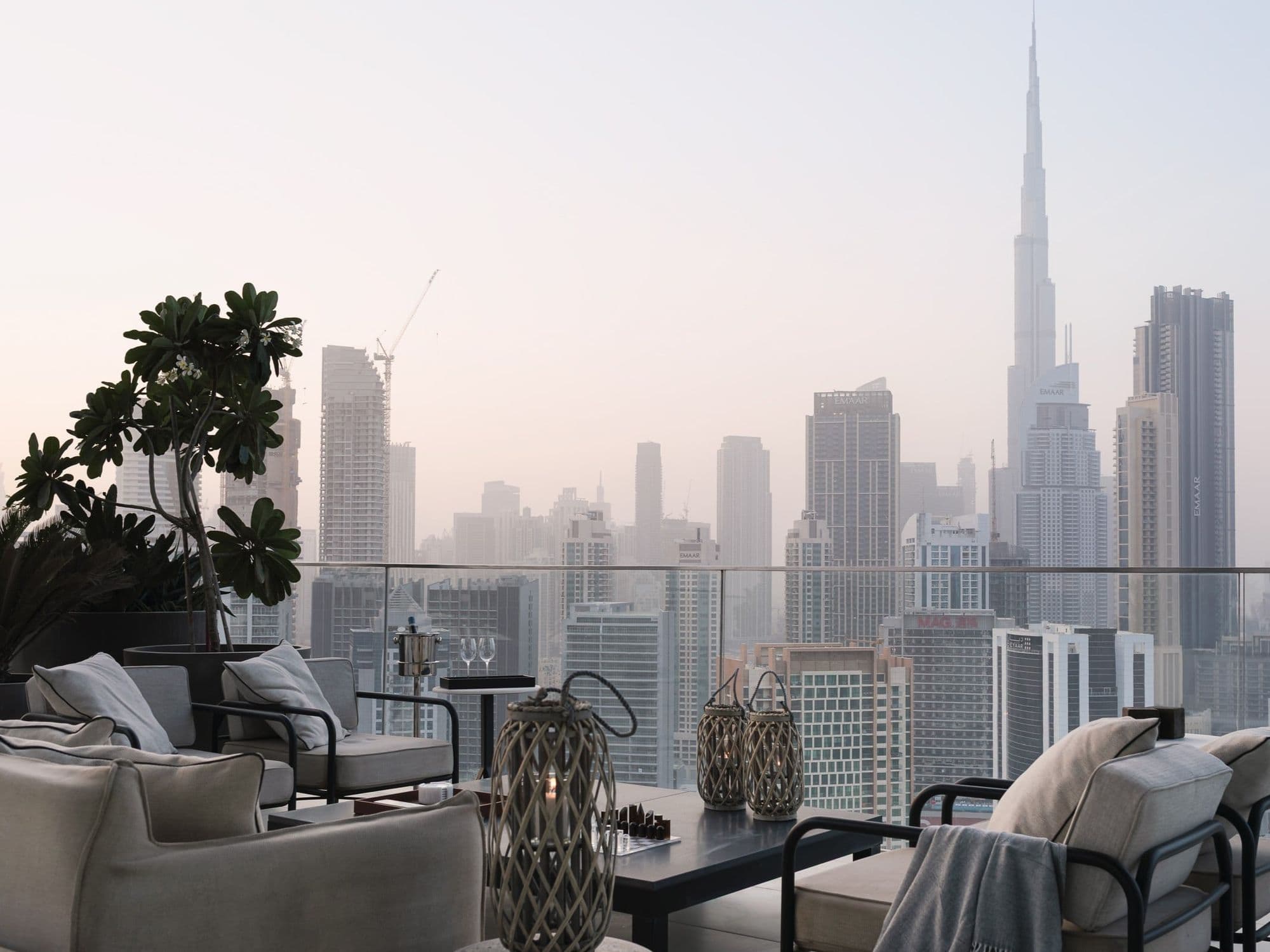 A terrace with outdoor sofas and lanterns, looking across Downtown Dubai to the Burj Khalifa.