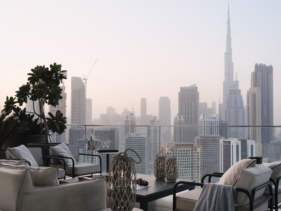 A terrace with outdoor sofas and lanterns, looking across Downtown Dubai to the Burj Khalifa.