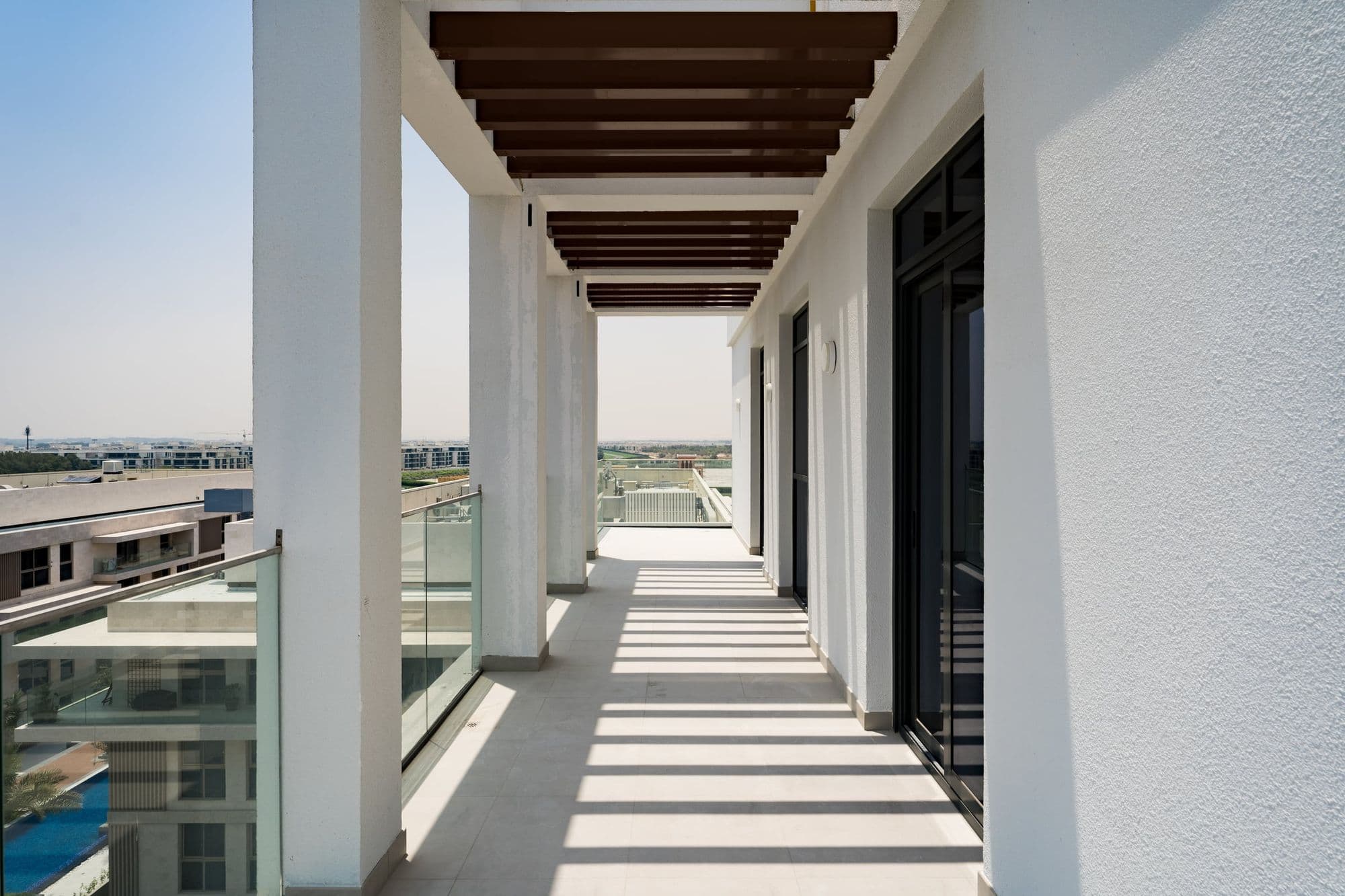 A long covered terrace with white columns and dark timber beams, the sun striping the floor.
