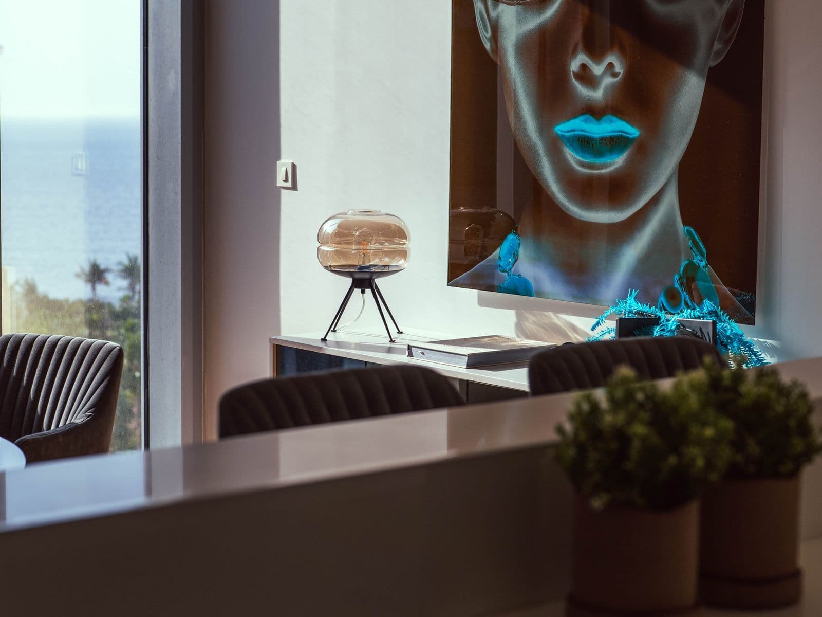 A living room with a large portrait painting on the wall and the sea through the windows beyond.