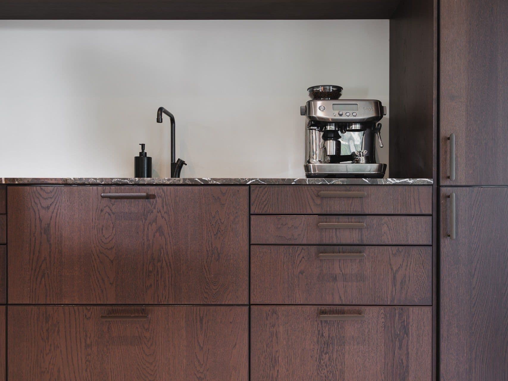 A dark oak kitchen with a black tap and an espresso machine on the counter.