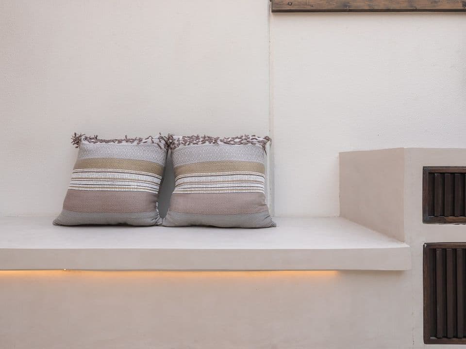 A built-in plaster bench with two striped cushions and a strip of warm light beneath it.