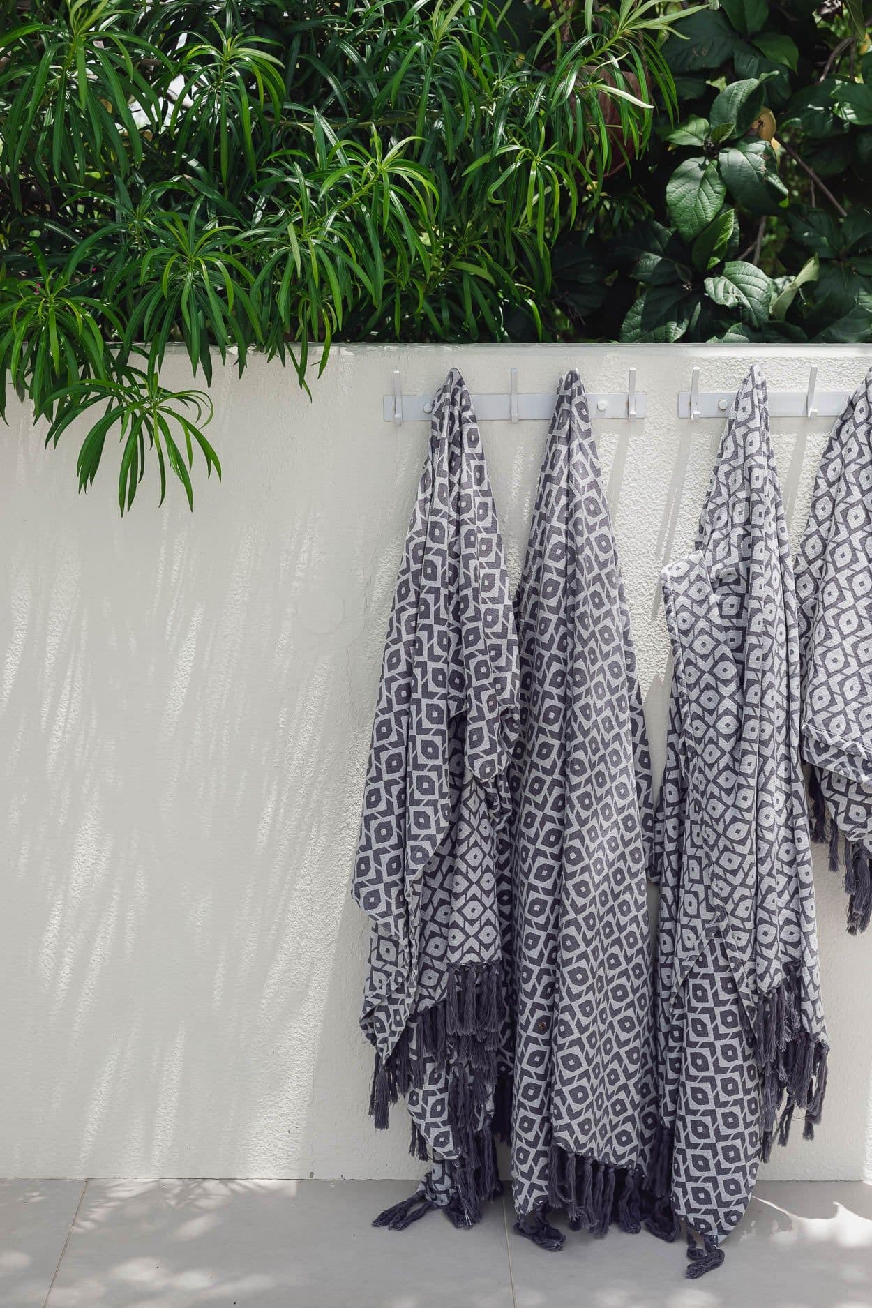 Patterned towels hanging from hooks on a white wall, under trailing green leaves.