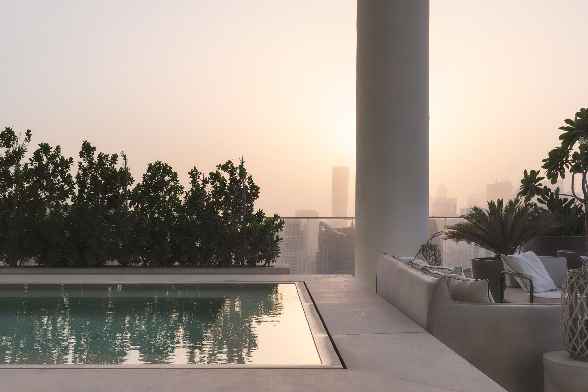 A rooftop pool at sunset, planting along its edge and towers in the haze beyond.