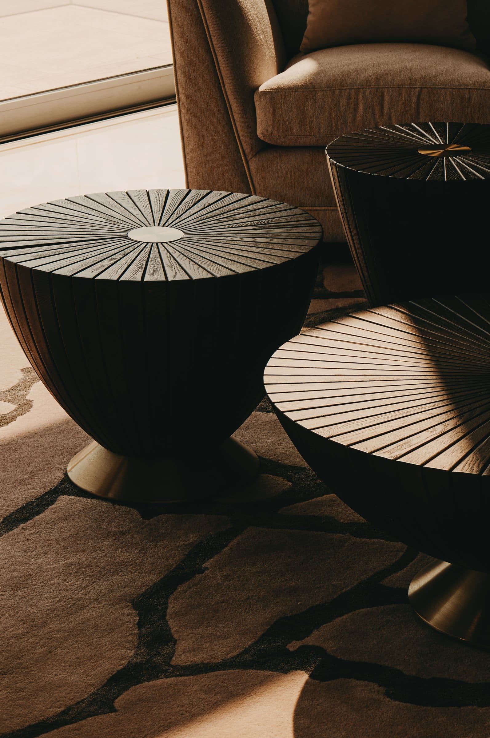 Two round timber side tables beside an armchair, in strong afternoon light.