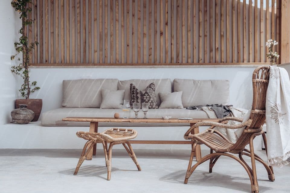 An outdoor lounge with a low timber table and a rattan armchair, against a slatted timber screen.