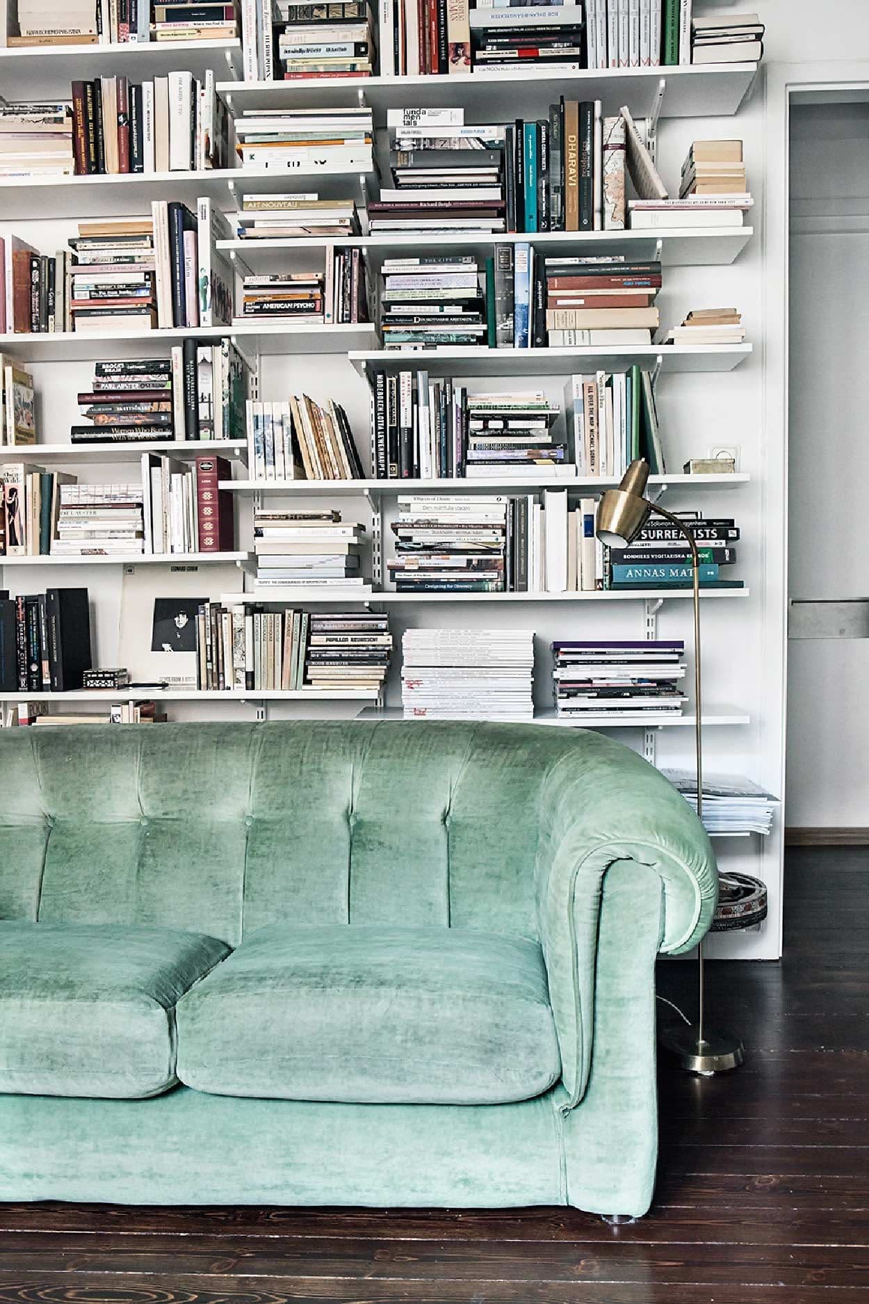 A green velvet Chesterfield sofa in front of wall-to-wall bookshelves.